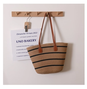 Close-up of woven straw tote bag with black stripes and brown leather shoulder straps