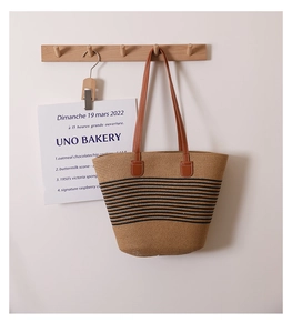 Detail of hand-woven straw tote with black stripes and brown leather shoulder straps