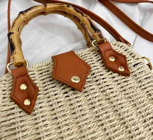 Détail du sac en paille montrant l'anse en bambou avec cuir marron et rivets dorés