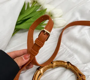 Détail de la bandoulière en cuir marron avec boucle dorée et poignée en bambou chic