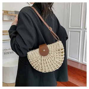 Detail of a straw crossbody bag with brown leather flap worn by a model in a blazer