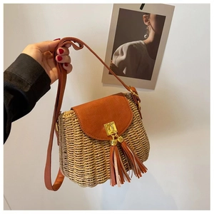 Detail of hand-woven straw crossbody bag with brown leather flap and tassel accents