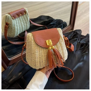 Detailed view of the straw crossbody bag featuring a brown leather tassel and gold buckle