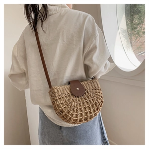 Detail of semi-circle straw bag featuring woven mesh texture and brown leather flap closure