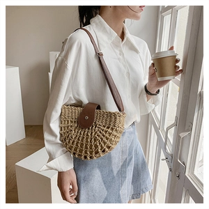 Detail of semicircular straw crossbody bag with brown leather strap worn by a model