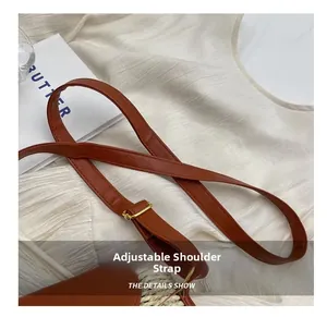 Detail of adjustable brown leather shoulder strap with gold metal buckle on woven bag