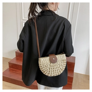 Detail of a semicircular straw crossbody bag with brown leather flap on a model