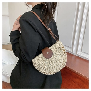 Detail view of woven straw half-moon bag with dark brown leather strap worn by a model