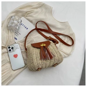 Detailed view of beige straw crossbody bag with brown leather flap and dual tassels