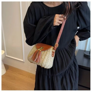 Detail of cream straw crossbody bag featuring brown leather fringe and adjustable strap