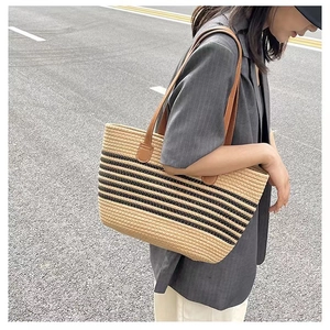 Close-up of a striped woven straw tote bag with brown PU leather handles in outdoor setting