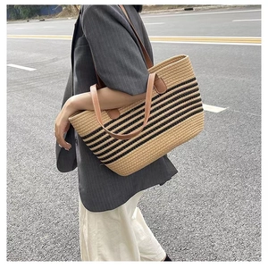 Detailed view of striped woven tote bag with brown leather handles in outdoor setting
