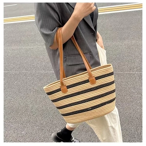 Detail of striped woven straw tote bag with brown leather handles on shoulder