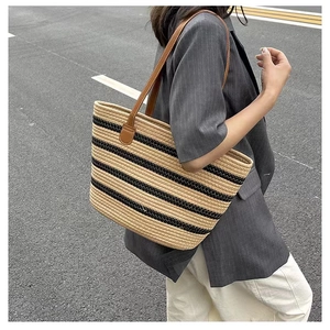 Detail of woven straw tote bag with black stripes and brown leather shoulder straps