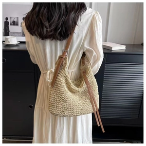 Close-up of beige woven straw tote bag with brown leather strap worn over the shoulder
