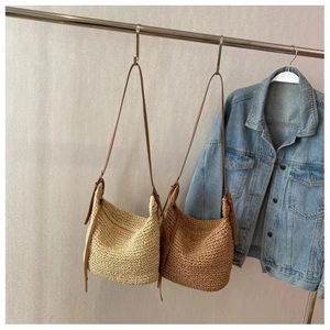Detail of handmade woven straw bags in beige and brown with slim leather shoulder straps