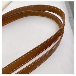 Close-up of brown leather shoulder strap with white contrast stitching on woven tote