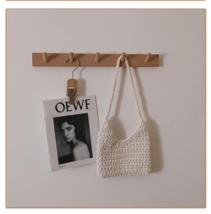 Detail of hand-woven cream cotton shoulder bag hanging on a minimalist wooden hook