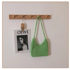 Close-up of light green hand-woven cotton shoulder bag hanging on a wooden wall hook
