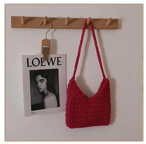 Detail of hand-woven magenta cotton crochet shoulder bag hanging on a wooden wall hook
