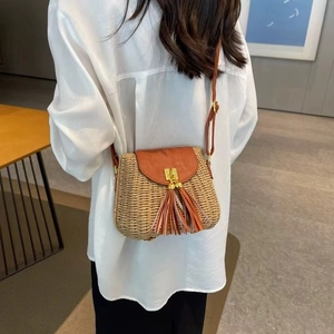 Straw crossbody bag with brown leather flap and tassel detail shown on a model