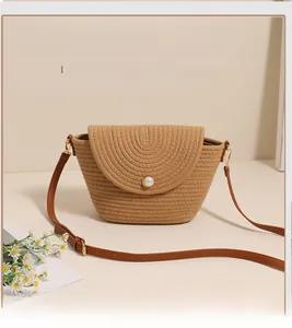 Detailed view of woven straw crossbody bag with pearl button and leather strap