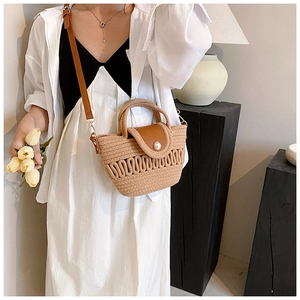 Detail of woven straw bag with brown leather flap, pearl accent, and shoulder strap