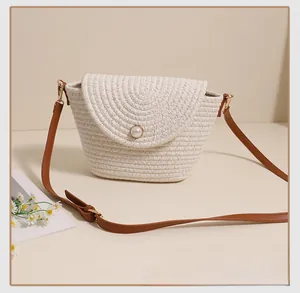 Close-up of white woven crossbody bag featuring a large pearl buckle and brown leather strap