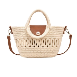Detail of woven straw handbag featuring brown leather flap and central pearl embellishment