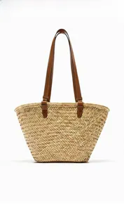 Detailed view of woven straw tote bag featuring sturdy brown leather handles and texture