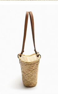 Detail of hand-woven straw bucket bag with brown leather straps and beige fabric lining