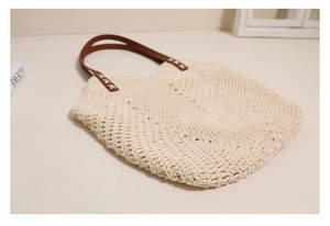 Detailed close-up of crochet hollow pattern and brown leather handles on a beige woven tote bag