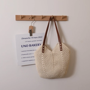 Beige cotton woven tote bag with brown leather shoulder strap on a wooden hook
