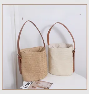 Detail of straw bucket bags in beige and cream with adjustable leather straps on table