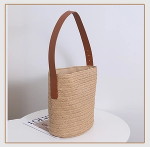 Detail of hand-woven straw bucket bag with adjustable brown leather shoulder strap