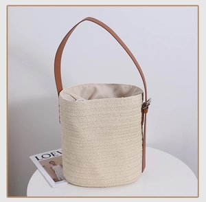 Detailed view of woven straw bucket bag with adjustable brown leather strap and fabric lining