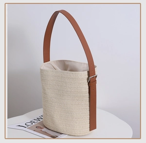 Detail of hand-woven straw bucket bag with brown leather strap and metal buckle