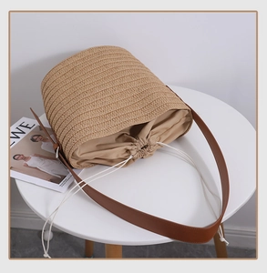Detailed close-up of straw woven shoulder bag featuring leather strap and drawstring lining