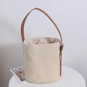 Minimalist straw bucket bag in cream white with brown leather strap on a white table