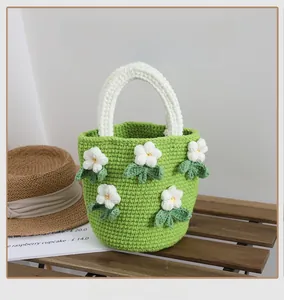Detailed view of handmade green knit bucket bag with white camellia flowers on wood