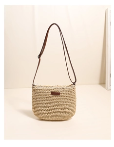 Close-up of woven straw crossbody bag with brown leather strap and minimalist patch