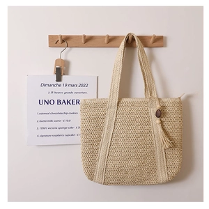 Detail of a beige woven tote bag with fringe charm hanging on a wooden hook
