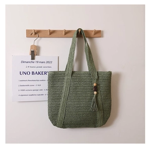 Close-up of green woven straw tote bag featuring decorative wooden bead tassel detail