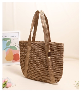 Detail of hand-woven straw tote bag with wood bead tassel hanging on beige background