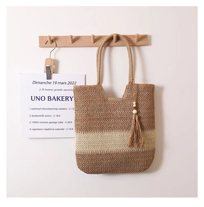 Detailaufnahme einer zweifarbigen Strohtasche mit Quasten an einem Holzhaken