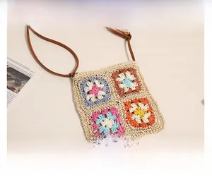 Detail of hand-crocheted square straw bag with colorful floral patterns and leather strap