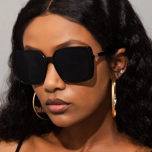 Detail of black oversized square sunglasses paired with gold sun hoop earrings on a model