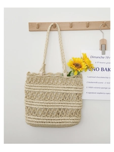 Close-up of beige woven straw tote bag with sunflower decoration hanging on a wooden hook