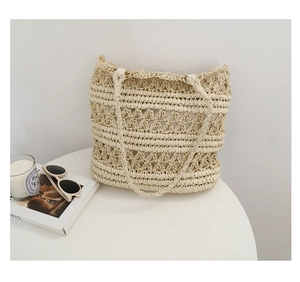 Close-up of beige crochet straw tote bag with hollow floral pattern on a white table