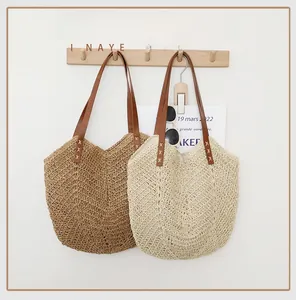 Détail de sacs fourre-tout en paille tressée avec anses en similicuir sur crochet